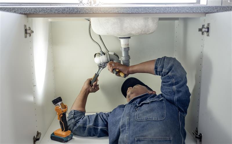 Plumber repairing pipes beneath a bathroom sink in Ontario