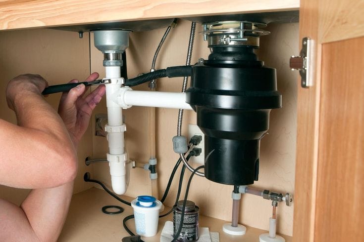 Plumber installing a garbage disposal beneath a kitchen sink in Ontario