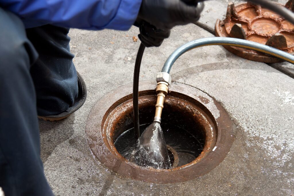 Plumber hydro jetting a sewer line through a manhole in Ontario