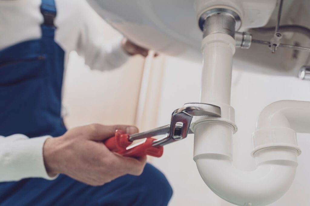 Plumber repairing a white drain pipe beneath a sink in Ontario