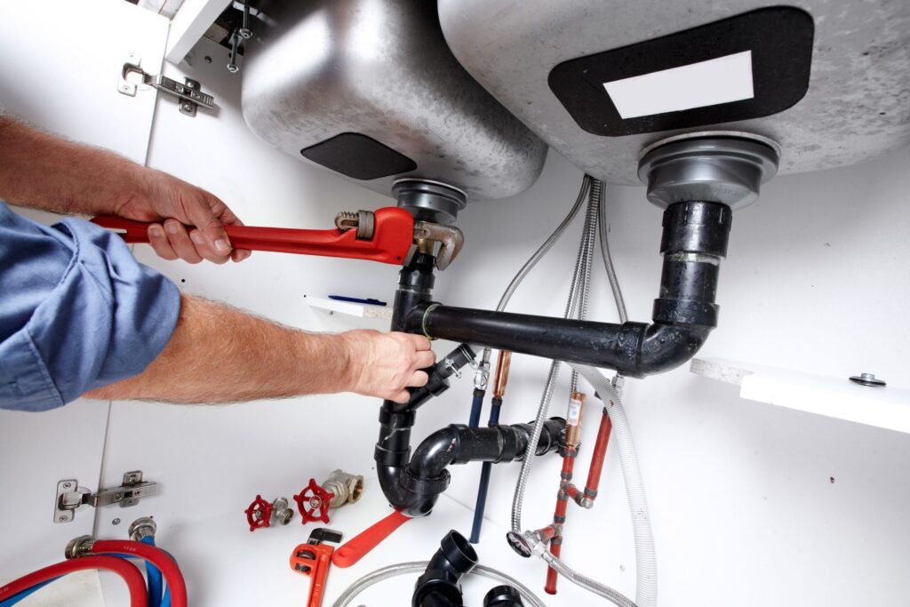 Plumber repairing drain pipes beneath a kitchen sink in Ontario